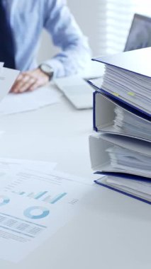 Ofis çalışanları mali raporları analiz ediyor ve ön planda evrak dolu mavi dosyalarla dolu beyaz bir masada otururken belgeleri imzalıyorlar. İş dünyasında denetim ve vergi teması