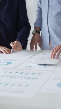 İş arkadaşları birlikte çalışıyor, finansal tabloları analiz ediyor ve bir ofis toplantısında şirket performansını tartışmak ve gelecekteki stratejileri planlamak için hesap makinesi kullanıyorlar..