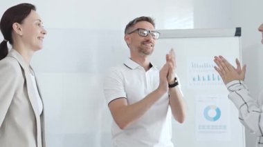 İş arkadaşları ofis toplantı odasında başarılı bir sunum yaptıktan sonra el çırpıyor, başarıyı ve takım çalışmasını kutluyorlar. İş adamları konsepti