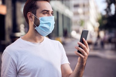 Açık havada akıllı telefonlu, gülümseyen bir adamın belden yukarı portresi.