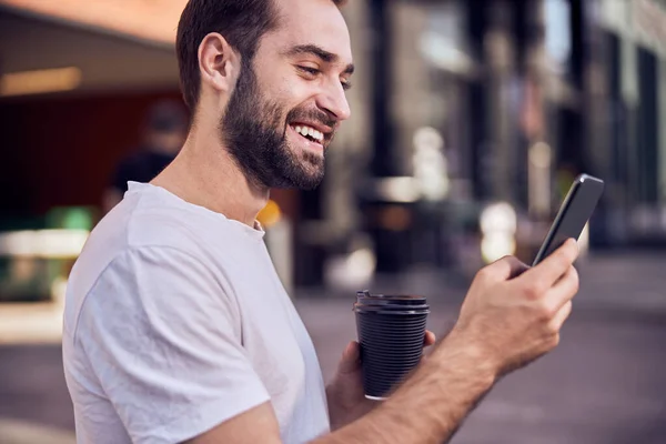 Waist up shot of fun man with coffee looking to smartphone