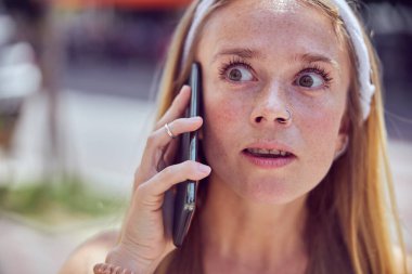 Kızıl saçlı, diş teli takan güzel bir kız akıllı telefonla konuşurken başka tarafa bakıyor.   