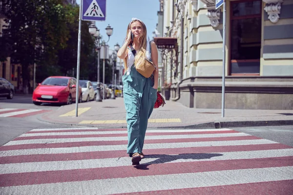   Çilli güzel, neşeli kız yaya geçidinde yürürken akıllı telefonla konuşuyor ve geleceğe bakıyor.