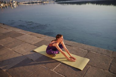 Sabahları dışarıda yoga yapan gülümseyen genç bir kadın.