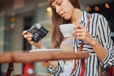 Kafede bir fincan kahveyle dinlenen ve kameradan çekilen fotoğraflara hayran olan genç ve güzel bir kadın fotoğrafçının kafası.