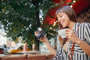 Kamera ve çay bardağıyla neşeli bir kadın.