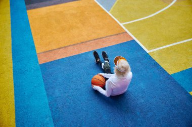 Dışarıda renkli bir meydanda basketbol topuyla yaşlı, sağlıklı ve neşeli bir bayan.