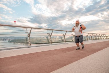 Şişman, beyaz sakallı ve cesur adam sabah egzersizleri yapıyor.