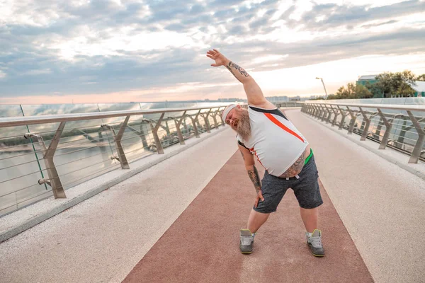 Fat caucasian bearded and bold man is doing morning exercses to loose his weight