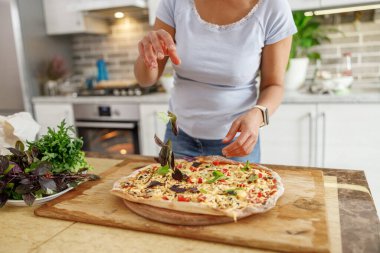 Güzel, hoş, yakışıklı bir kadın evdeki mutfağında sebzeli taze İtalyan pizzası hazırlıyor.