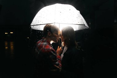 Bir adam ve bir kadın yağmur sırasında şemsiye altında sokakta öpüşürler. Aşk ve romantizm kavramı