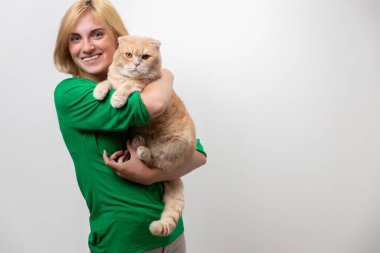 Çekici bir kadının stüdyo portresi. Diş telleri elinde, beyaz bir arka planda kediyi tutan.