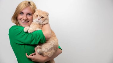 Çekici bir kadının stüdyo portresi. Diş telleri elinde, beyaz bir arka planda kediyi tutan.