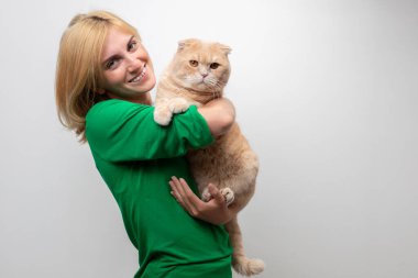 Çekici bir kadının stüdyo portresi. Diş telleri elinde, beyaz bir arka planda kediyi tutan.