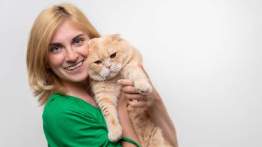 Çekici bir kadının stüdyo portresi. Diş telleri elinde, beyaz bir arka planda kediyi tutan.