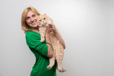 Çekici bir kadının stüdyo portresi. Diş telleri elinde, beyaz bir arka planda kediyi tutan.