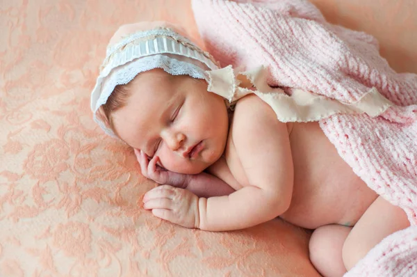 安静的婴儿躺在床上 睡在明亮的白光室里 女孩用毯子裹着一条针织保暖毯 在一个粉红色的花边背景在一个可爱的帽子 — 图库照片