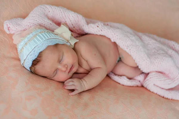安静的婴儿躺在床上 睡在明亮的白光室里 女孩用毯子裹着一条针织保暖毯 在一个粉红色的花边背景在一个可爱的帽子 — 图库照片