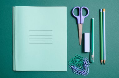 Set of school supplies with notebook, pen, pencil, scissors and clips. School supplies, colored pencils on a green background. Scissors and compasses, blue ruler. copy space clipart