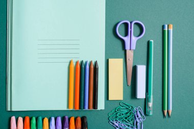Okul malzemeleri defter, kalem, kurşun kalem, makas ve klipler ile kümesi. Okul malzemeleri, yeşil bir arka plan üzerinde renkli kalemler. Makas ve pergel, mavi cetvel. kopya alanı