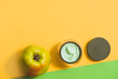 yüz kremi, yeşil elma, sarı papatya parlak bir arka plan üzerinde. Açık bir kavanoz içinde taze çiçekler ile doğal kozmetik