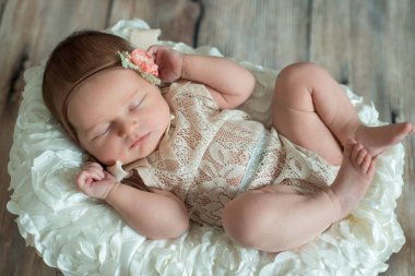 Yeni doğan bebek kız, hasır sepet bej ahşap zemin üzerinde ekose şal üzerinde uyuyan bandaj yay.