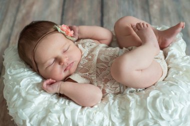 Yeni doğan bebek kız, hasır sepet bej ahşap zemin üzerinde ekose şal üzerinde uyuyan bandaj yay.