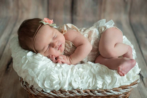Yeni doğan bebek kız, hasır sepet bej ahşap zemin üzerinde ekose şal üzerinde uyuyan bandaj yay.
