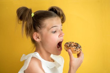 Güzel genç kız çörek yeme. ağzını açık ısırığı. duygusal gülüyor. sarı yak arka plan. yaz güneşli resim