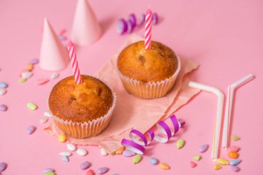 İki çikolatalı kek, Doğum günü mumu. Parti kızlar için. Kapaklar ve tinsel ve pembe bir arka plan üzerinde çok renkli tatlılar