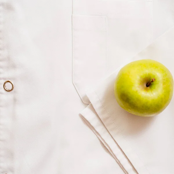 an apple lies on a white medical dressing gown.