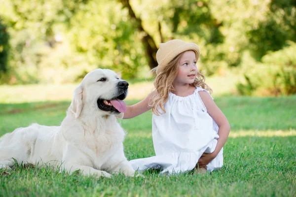 Küçük şirin yürümeye başlayan çocuk sarışın kız büyük beyaz çoban köpeğiyle oynuyor. Seçici odak