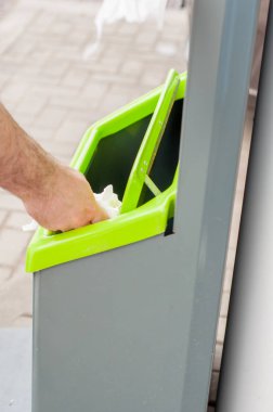 Çöp tenekesine bir çöp parçası tutan Closeup el