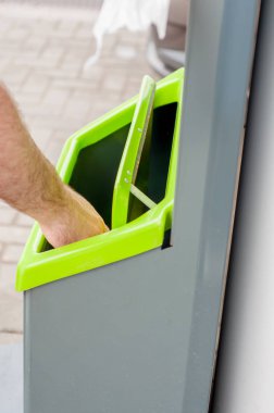 Çöp tenekesine bir çöp parçası tutan Closeup el