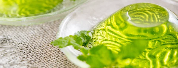 Green jelly with mint leaves in glass on wooden background. Juice with ice in gelatin. on a linen napkin on a white background. Long wide banner.