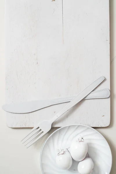 White fork knife plate on an old wooden plank tray ,art abstract absurdity idea white tomatoes, all in one color