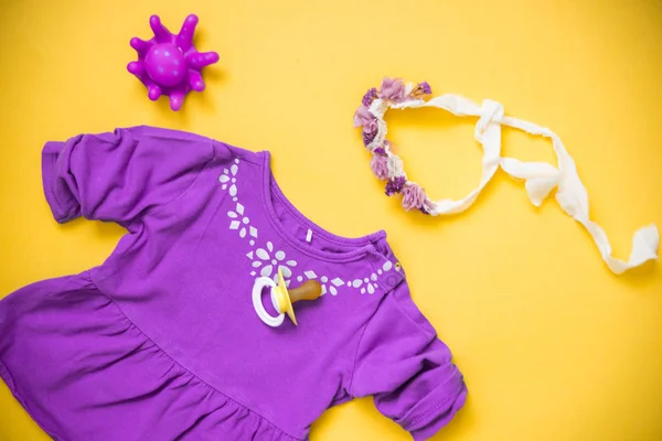 Baby Purple clothes and necessities on yellow background. A dummy and a wreath a bandage on the head