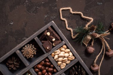 Noel kompozisyon koyu arka plan üzerinde. Fındıklı, dekoratif ahşap kutu şeker bir altın paketinde, çikolata, koni ve ladin yüzyılların parçalar