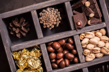 Noel kompozisyon koyu arka plan üzerinde. Fındıklı, dekoratif ahşap kutu şeker bir altın paketinde, çikolata, koni ve ladin yüzyılların parçalar