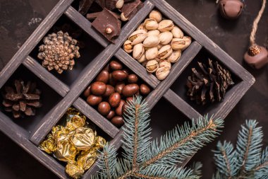Noel kompozisyon koyu arka plan üzerinde. Fındıklı, dekoratif ahşap kutu şeker bir altın paketinde, çikolata, koni ve ladin yüzyılların parçalar