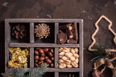Noel kompozisyon koyu arka plan üzerinde. Fındıklı, dekoratif ahşap kutu şeker bir altın paketinde, çikolata, koni ve ladin yüzyılların parçalar