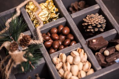 Noel kompozisyon koyu arka plan üzerinde. Fındıklı, dekoratif ahşap kutu şeker bir altın paketinde, çikolata, koni ve ladin yüzyılların parçalar