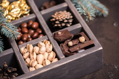 Noel kompozisyon koyu arka plan üzerinde. Fındıklı, dekoratif ahşap kutu şeker bir altın paketinde, çikolata, koni ve ladin yüzyılların parçalar