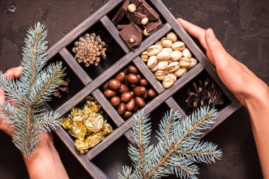 Noel kompozisyon koyu arka plan üzerinde. Fındıklı, dekoratif ahşap kutu şeker bir altın paketinde, çikolata, koni ve ladin yüzyılların parçalar. Bir hediye holding eller