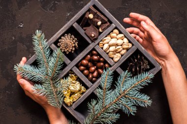 Noel kompozisyon koyu arka plan üzerinde. Fındıklı, dekoratif ahşap kutu şeker bir altın paketinde, çikolata, koni ve ladin yüzyılların parçalar. Bir hediye holding eller