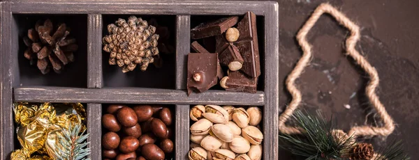 Uzun banner. Noel kompozisyon koyu arka plan üzerinde. Fındıklı, dekoratif ahşap kutu şeker bir altın paketinde, çikolata, koni ve ladin yüzyılların parçalar