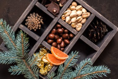 Noel kompozisyon koyu arka plan üzerinde. Fındıklı, dekoratif ahşap kutu şeker bir altın paketinde, çikolata, koni ve ladin yüzyılların parçalar
