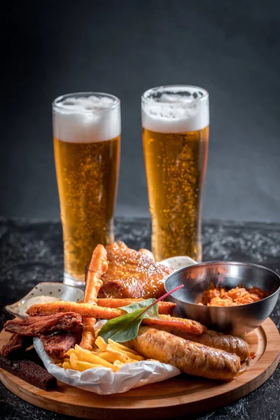 Foamy beer in a glass, hot appetizer, chicken wings, sauce in a beautiful served bowl. Catrofel and other deep-fried vegetables. unhealthy food. unhealthy food. many calories