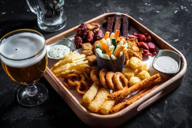 Çeşitli bira aperatifler - sosis, tavuk kanatları, kruton, soğan halkaları ve ahşap tahta sos ile kalamar halkaları ve bardak bira kümesi