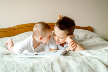 İki çocuk, bir beyaz yatakta kendilerini eğitmek kitap okumak gülüyor ve birlikte gülüyor sevimli sarışın kız ve erkek çocuklar